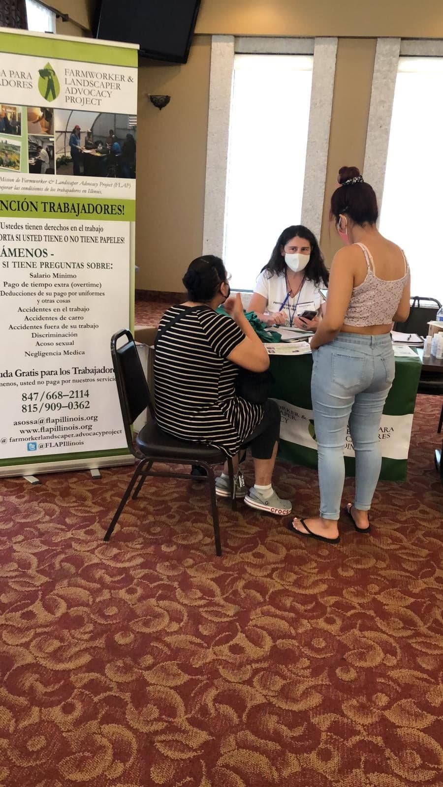 FLAP staff meet with two women at the organization's table at an indoor resource fair.