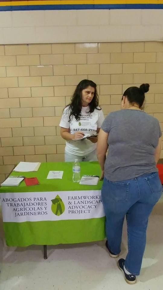 A FLAP staff member takes notes with a visitor at the organization's table in a school gymnasium.