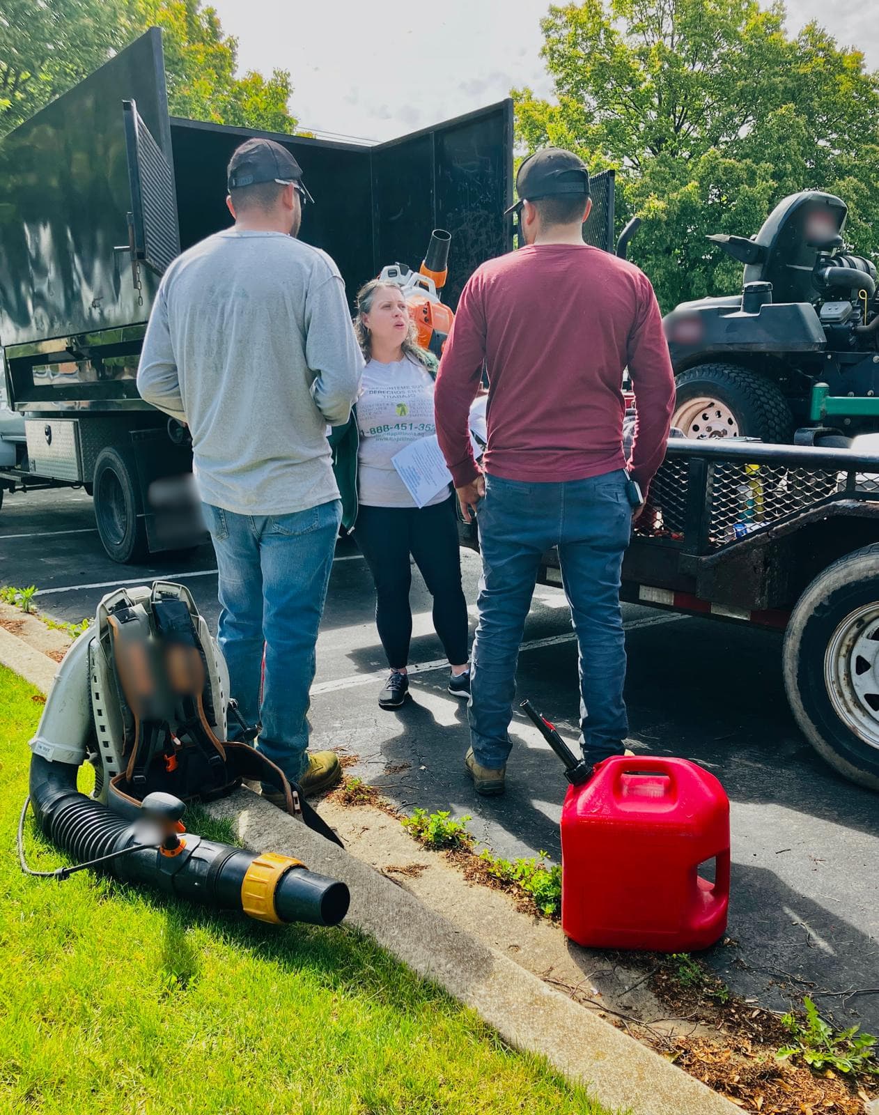 A FLAP outreach worker hands know-your-rights flyers to two landscapers standing between their truck and a trailer of mowing equipment.