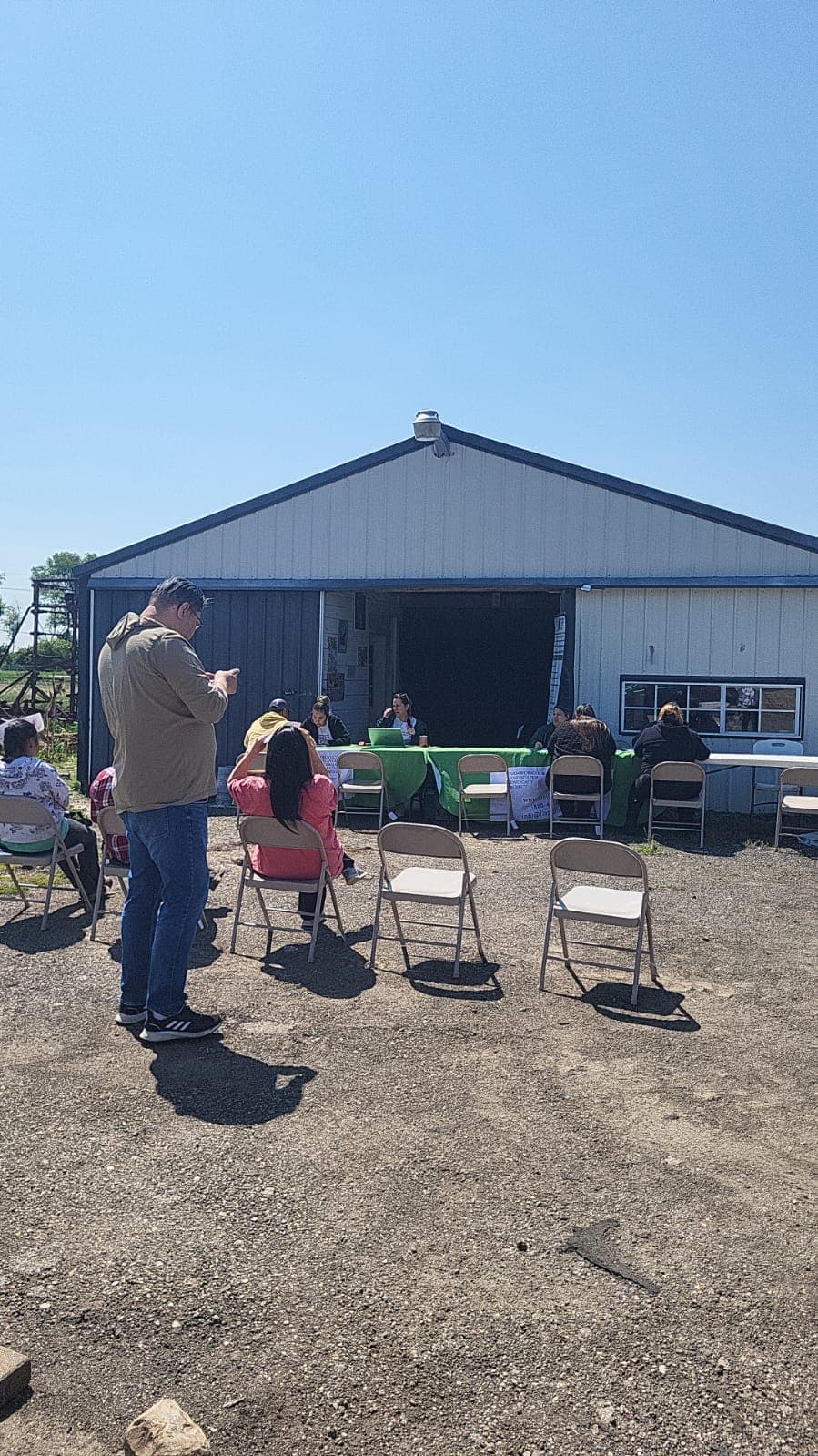 Workers sit in folding chairs facing FLAP's outdoor information table at a farm.