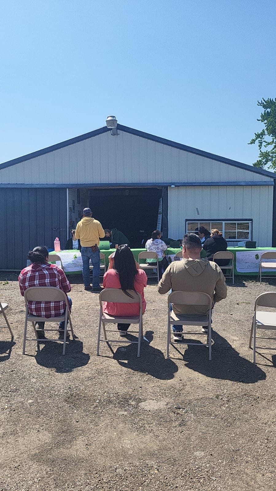 Workers seated outdoors listen to a FLAP presentation in front of a farm shed.
