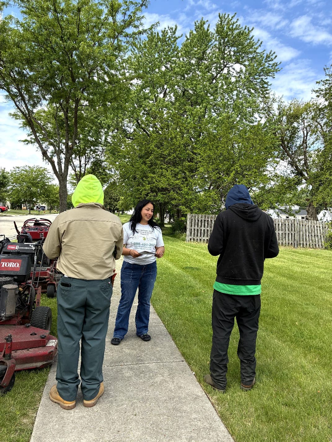 A FLAP outreach worker talks with two landscapers on a residential sidewalk beside their mower.
