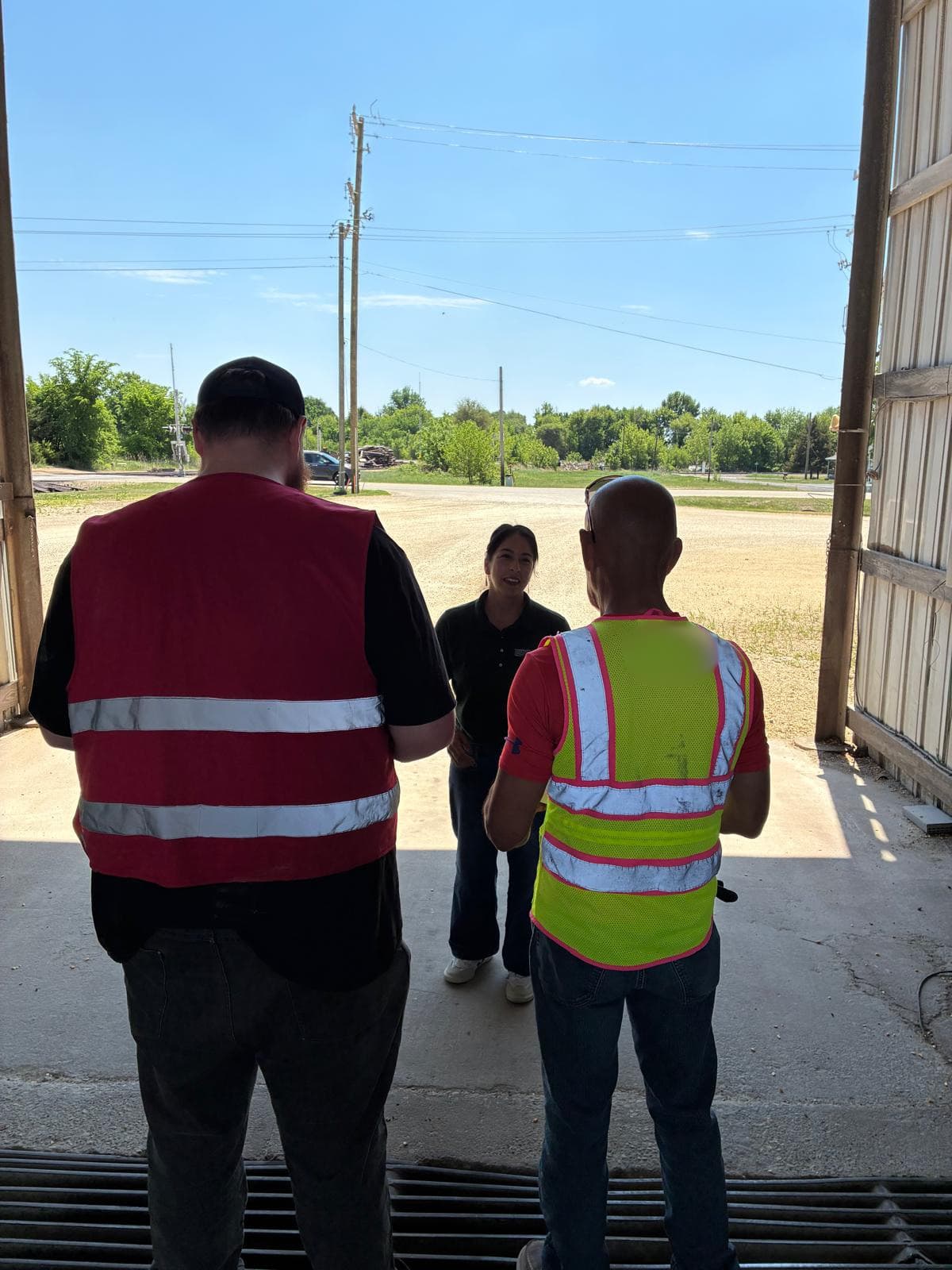 A FLAP outreach worker talks with two workers in high-visibility vests in the doorway of a work building.