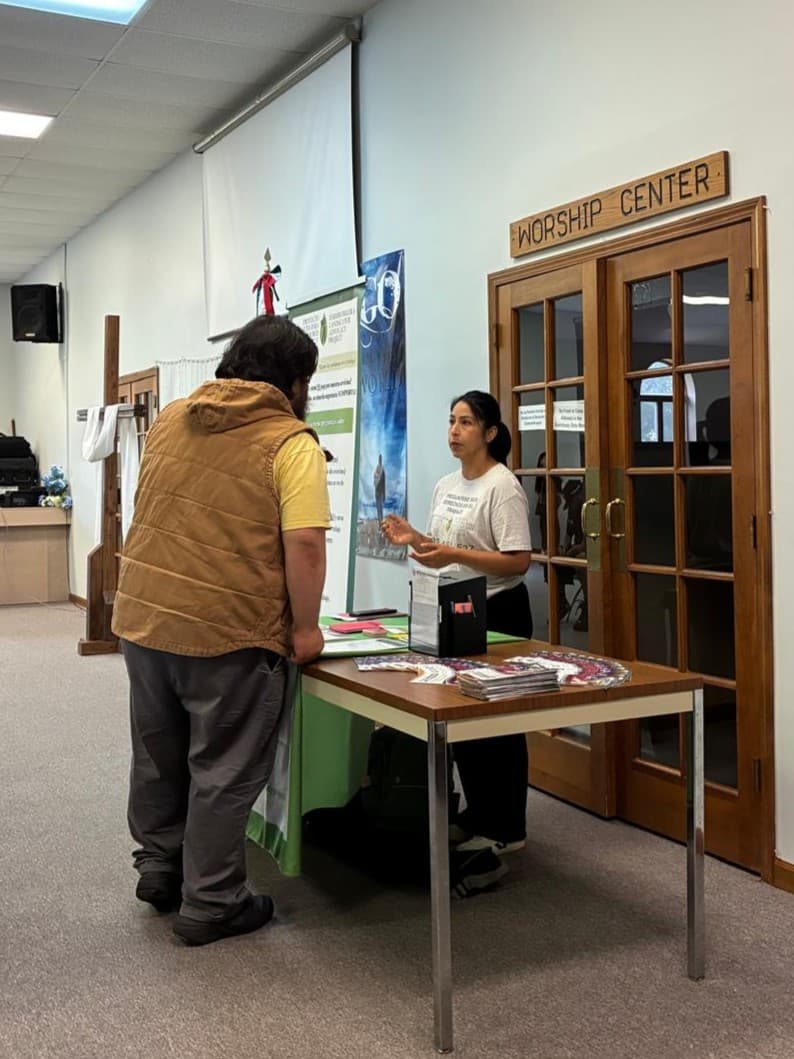 A FLAP staff member talks with a visitor at an information table set up in a church lobby.