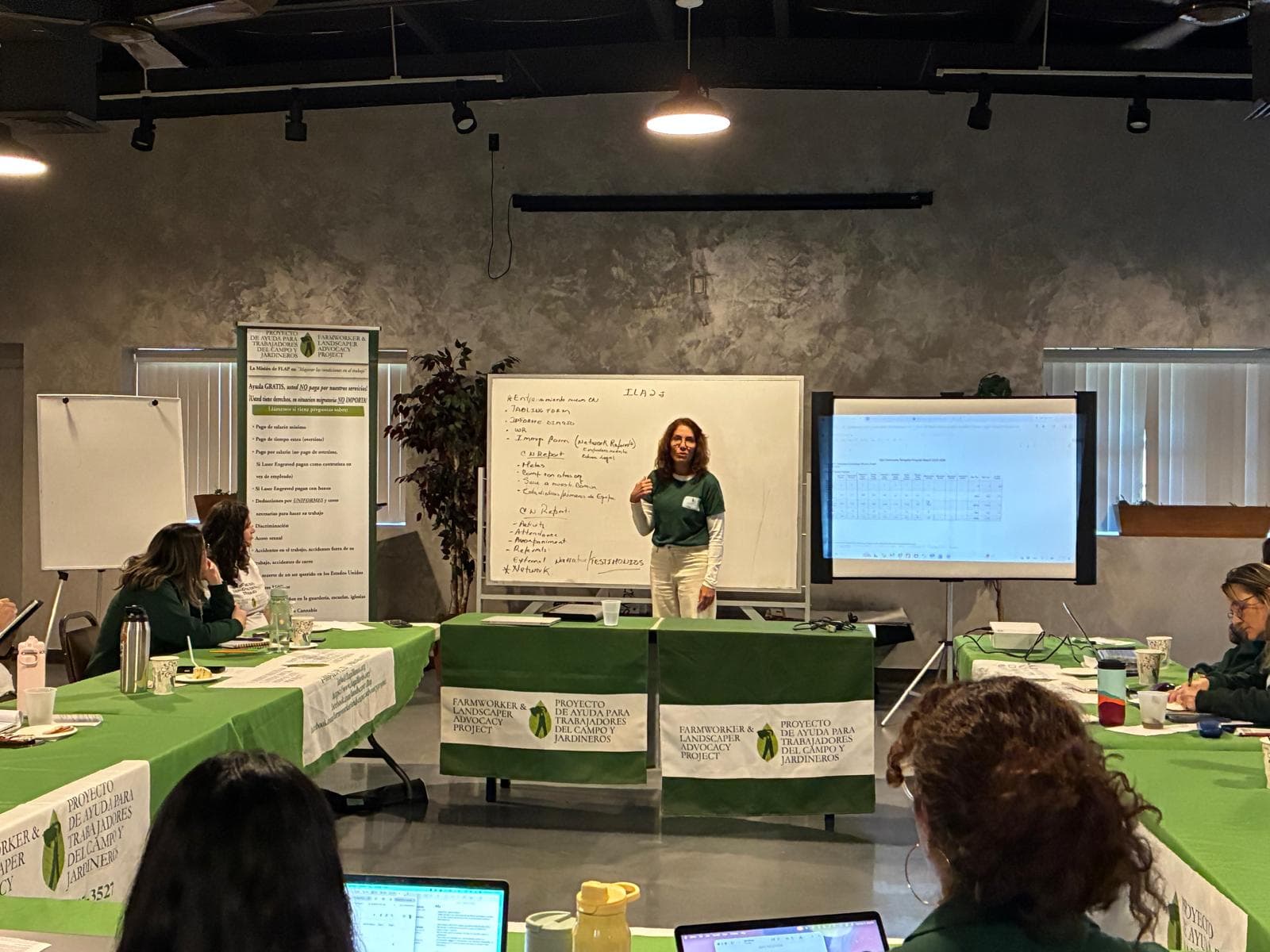 A FLAP staff member leads a team training at a whiteboard, with colleagues seated at tables draped in FLAP banners.