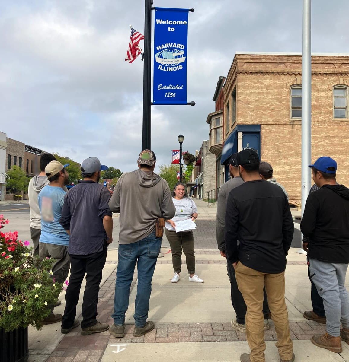 A FLAP outreach worker talks with a group of landscapers on a downtown sidewalk in Harvard, Illinois.
