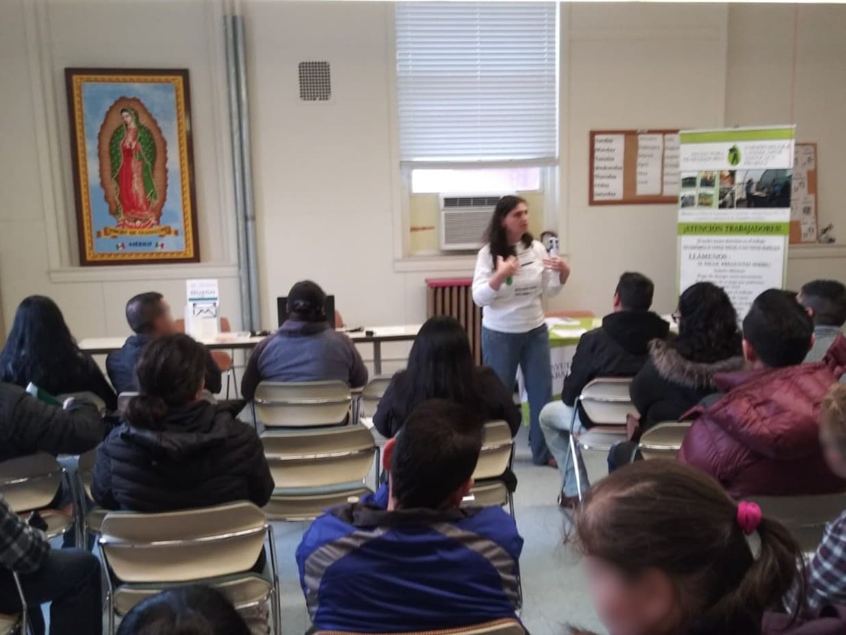 A FLAP staff member addresses a full room of workers at a community meeting.