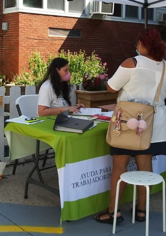 A FLAP staff member helps a visitor at an outdoor information table at a community event.